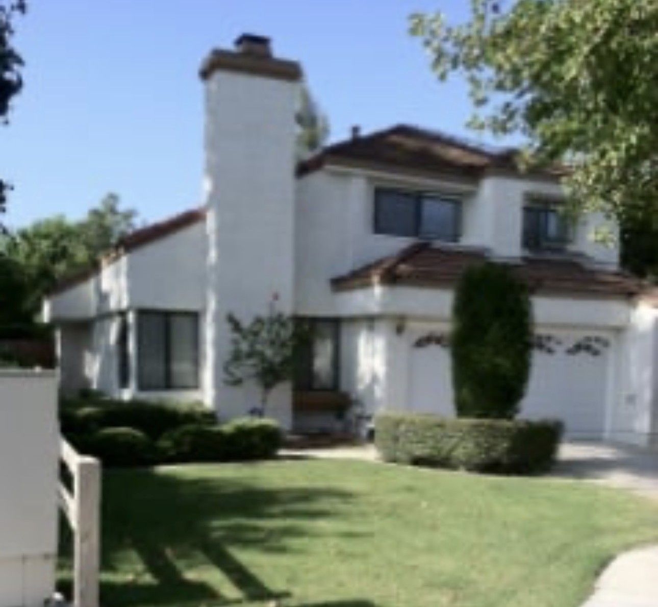 Suburban two-story white house with chimney, green lawn, and garage under a clear blue sky
