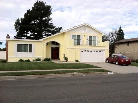 Suburban two-story yellow house with a garage and a red car parked in the driveway
