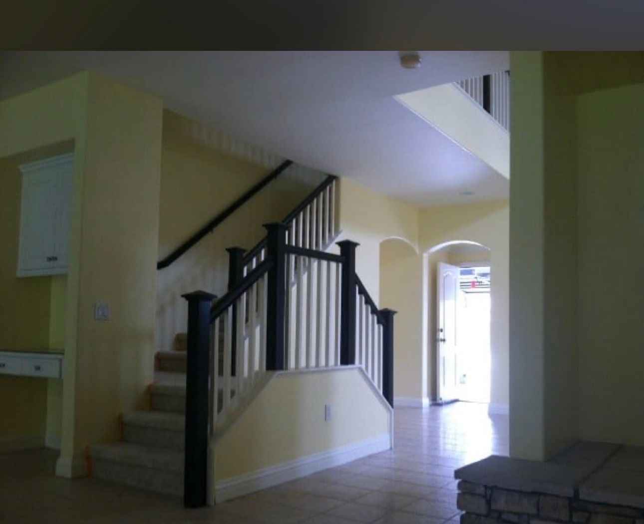 Interior staircase with dark railing, beige walls, and tiled floor leading to a bright hallway