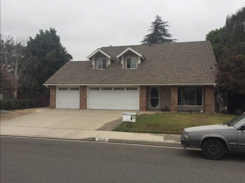 Suburban brick house with three garage doors and a driveway, viewed from the street