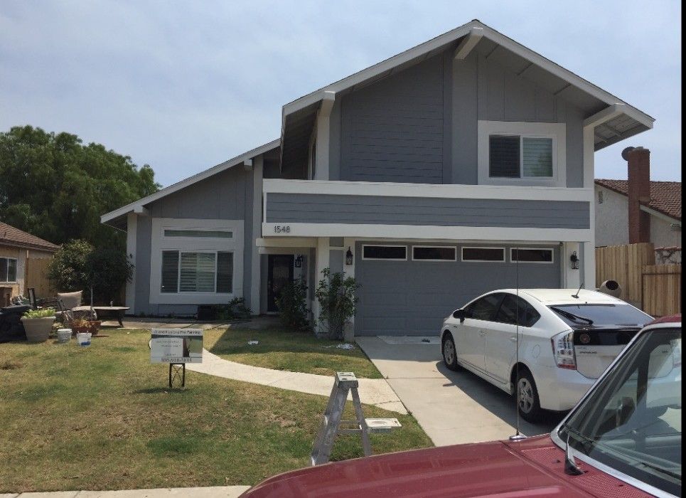 Modern gray two-story house with a white car parked in the driveway and a front lawn.