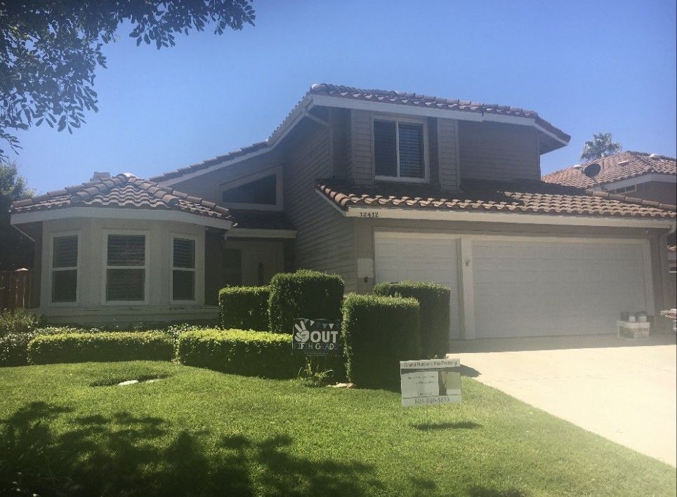 Suburban house with a tiled roof, manicured hedges, and a two-car garage in bright sunlight