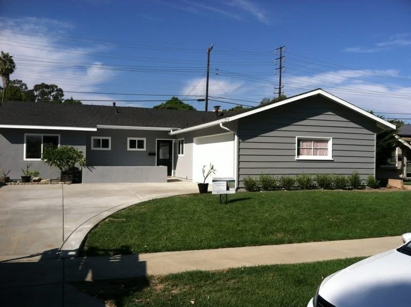 Single-story gray house with driveway, green lawn, and clear blue sky