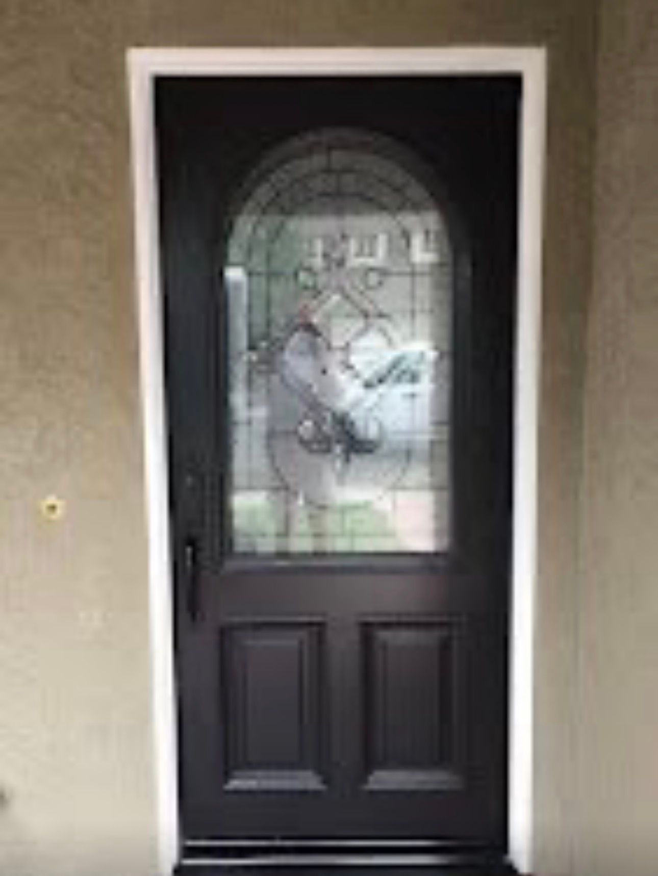 Black front door with arched glass window in a beige exterior wall