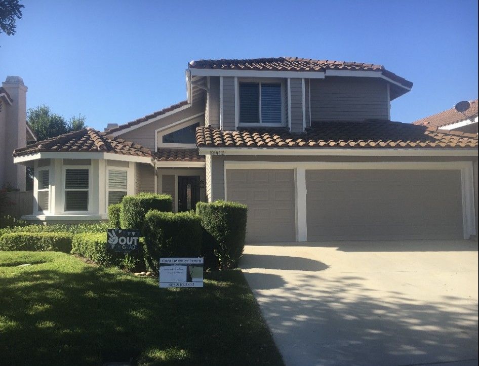 Two-story suburban house with beige stucco, red-tile roof, and a double garage under a blue sky