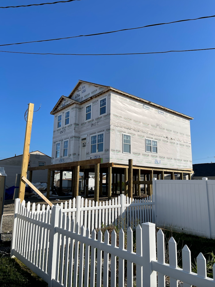 A white picket fence surrounds a house under construction