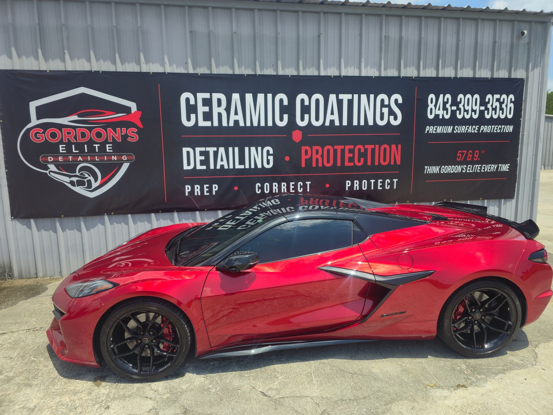 Red sports car parked in front of a ceramic coatings and detailing shop banner
