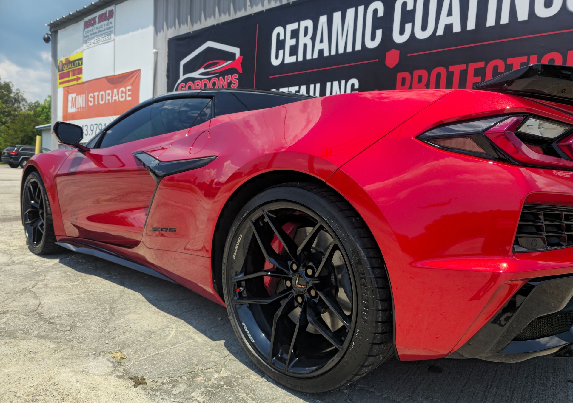 Red sports car with black rims parked outside a ceramic coating shop.