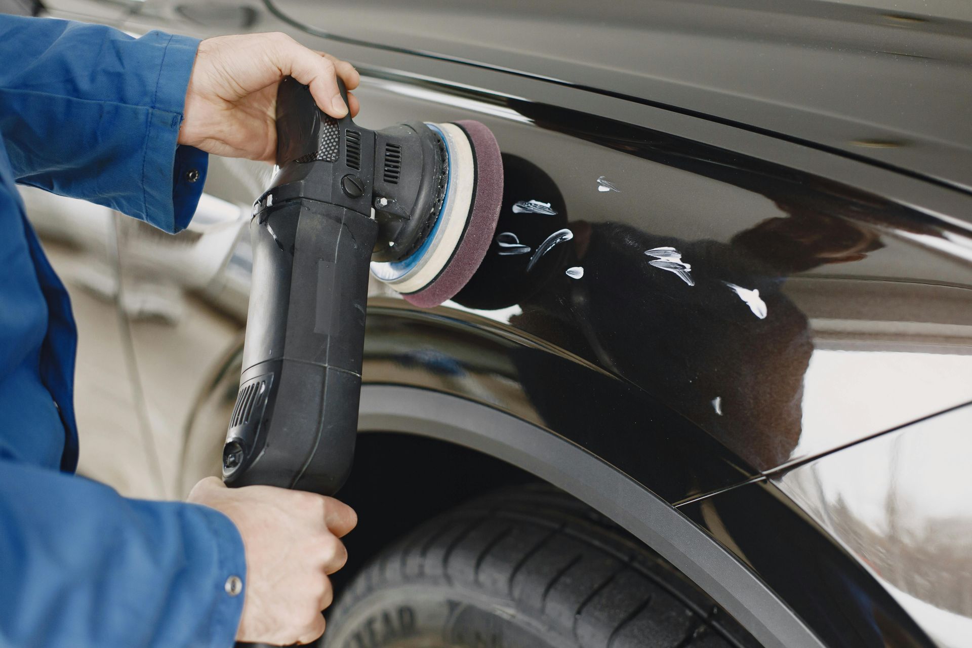 A man is polishing a black car with a machine