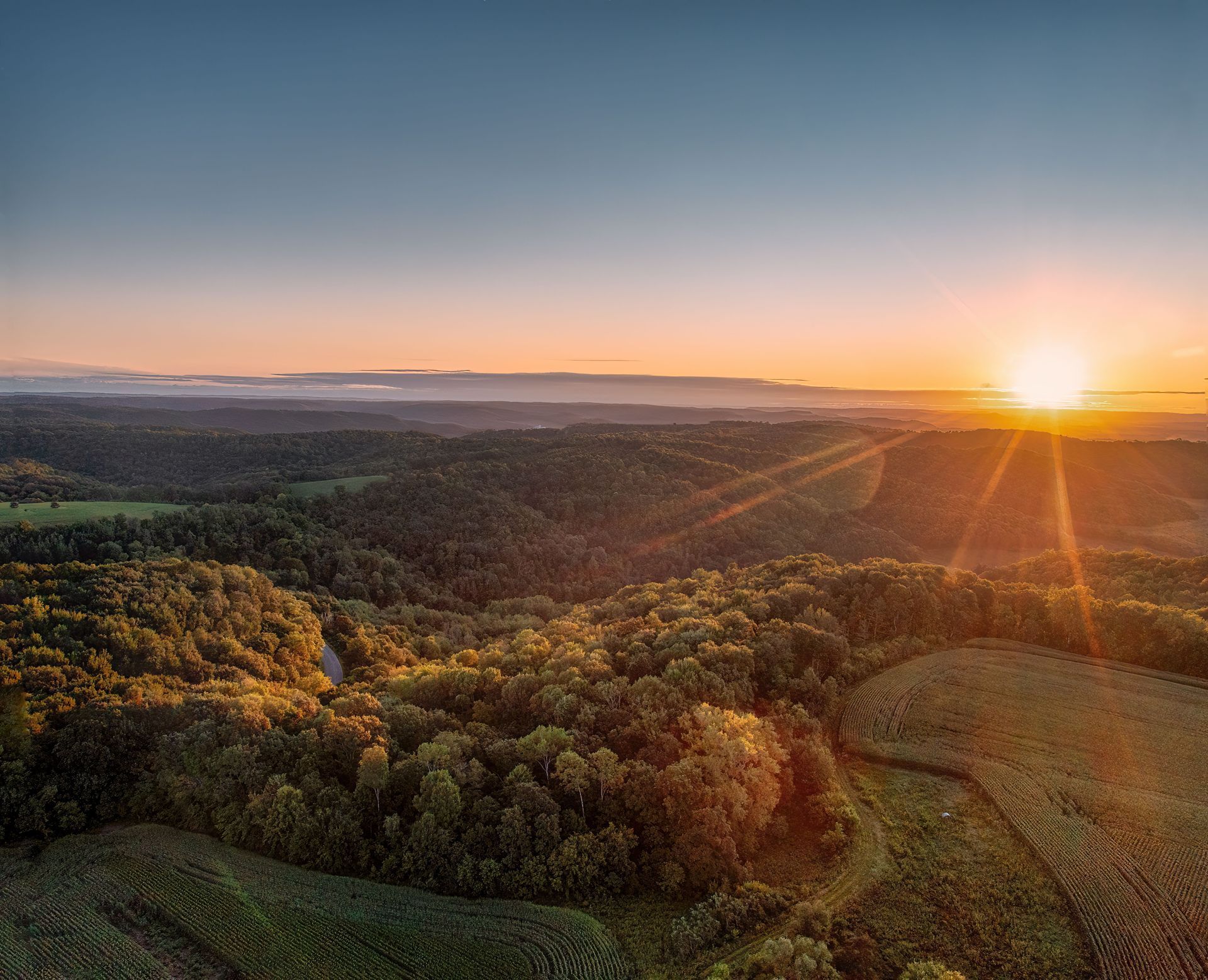 Sunset over rolling forested hills with warm orange light and a hazy horizon