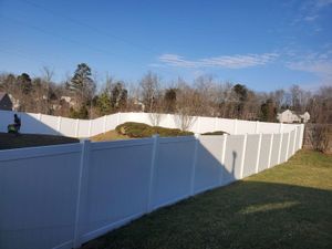 White vinyl fence along a grassy yard under a clear blue sky, with trees and houses in the background