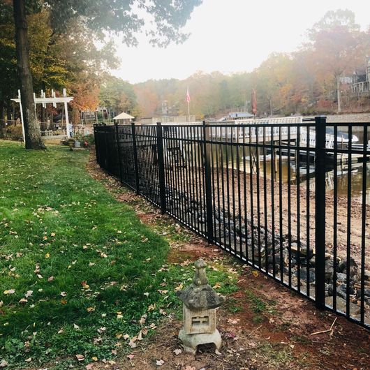 Tree-lined park path beside a black iron fence, with autumn leaves and soft morning light.