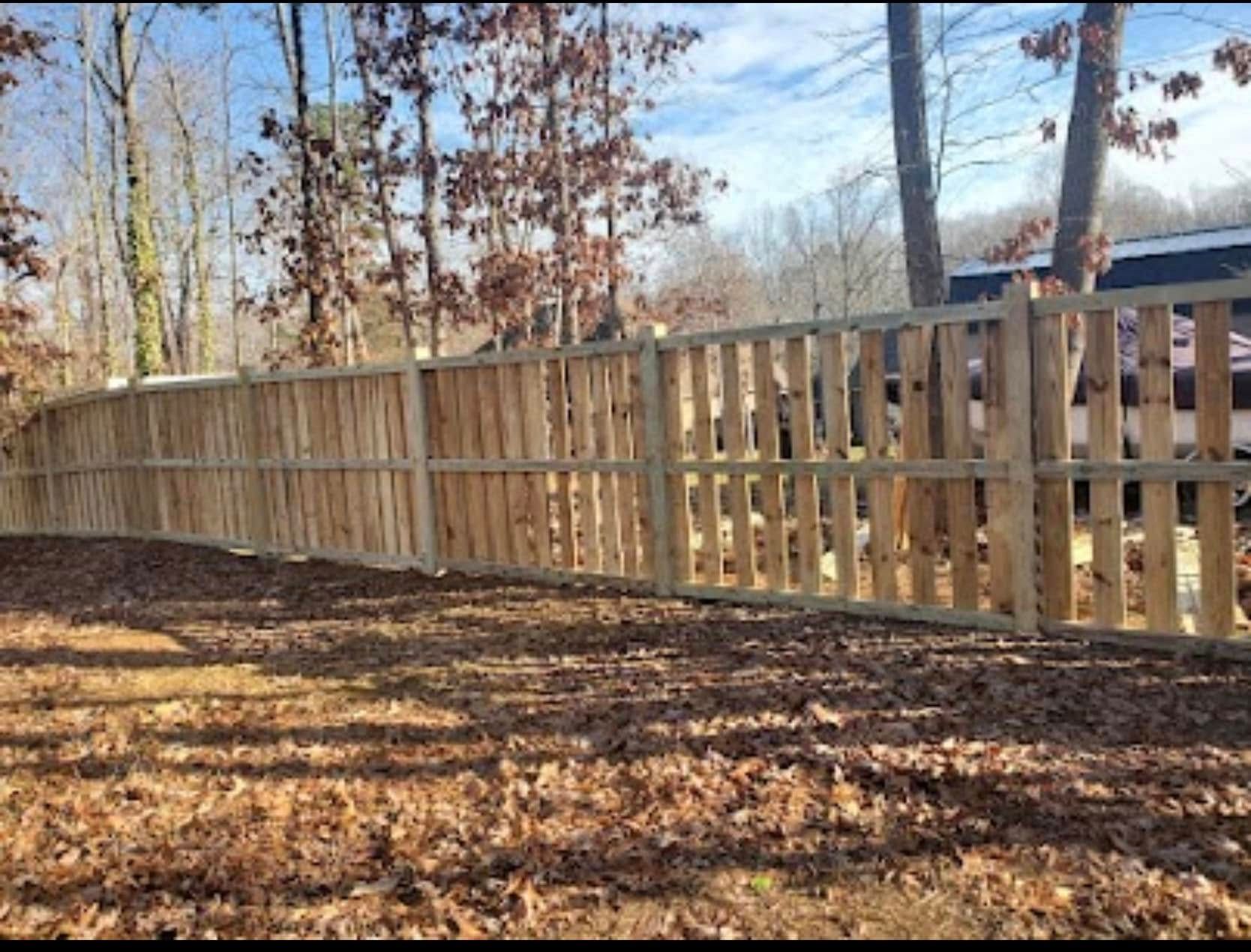 Wooden privacy fence along a leaf-covered yard with bare trees in the background.
