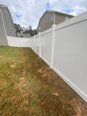 White vinyl fence along a grassy backyard beside suburban houses under a cloudy sky