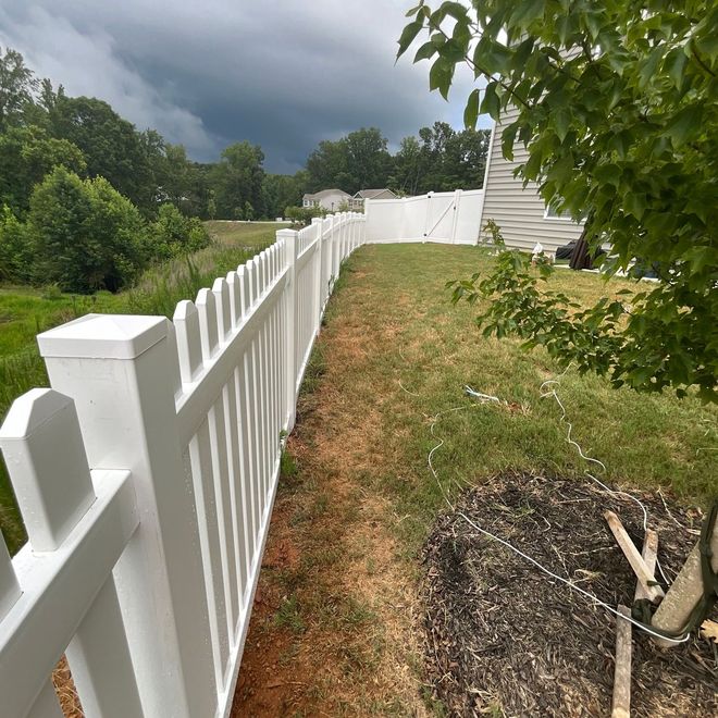 White picket fence beside a grassy yard under dark storm clouds