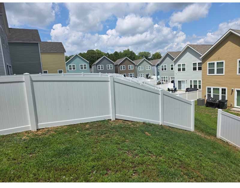 White vinyl fence enclosing a grassy yard in a suburban neighborhood with houses and cloudy sky