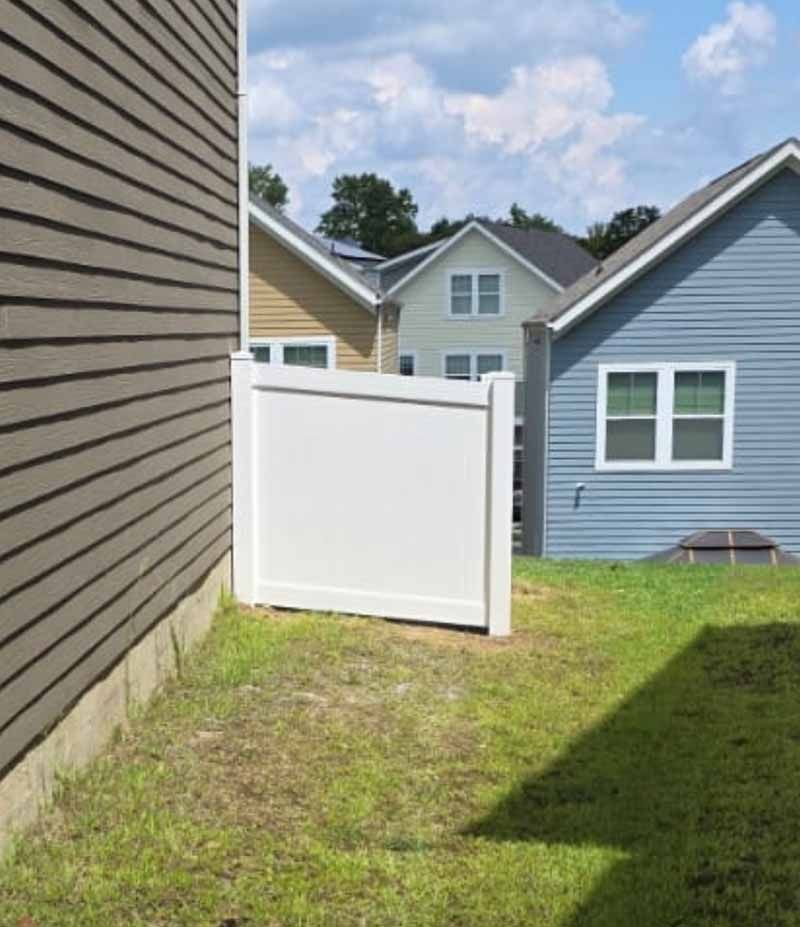 Backyard with white fence gate between houses, green lawn, and blue sky.