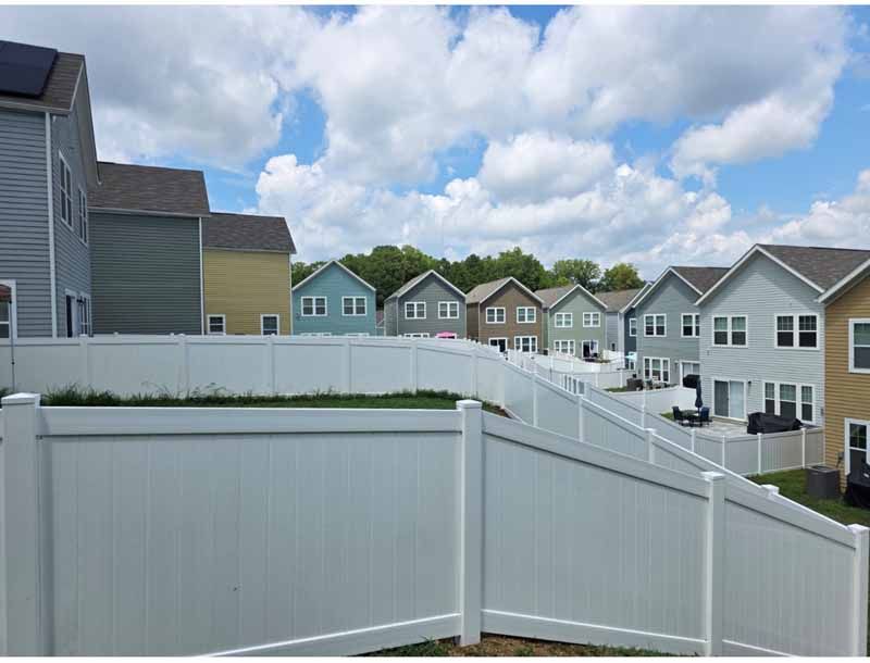 Row of suburban houses behind a white fence under a partly cloudy sky