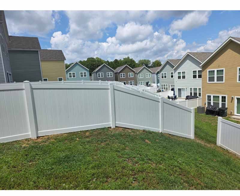White vinyl fence around a grassy yard with row houses under a partly cloudy sky
