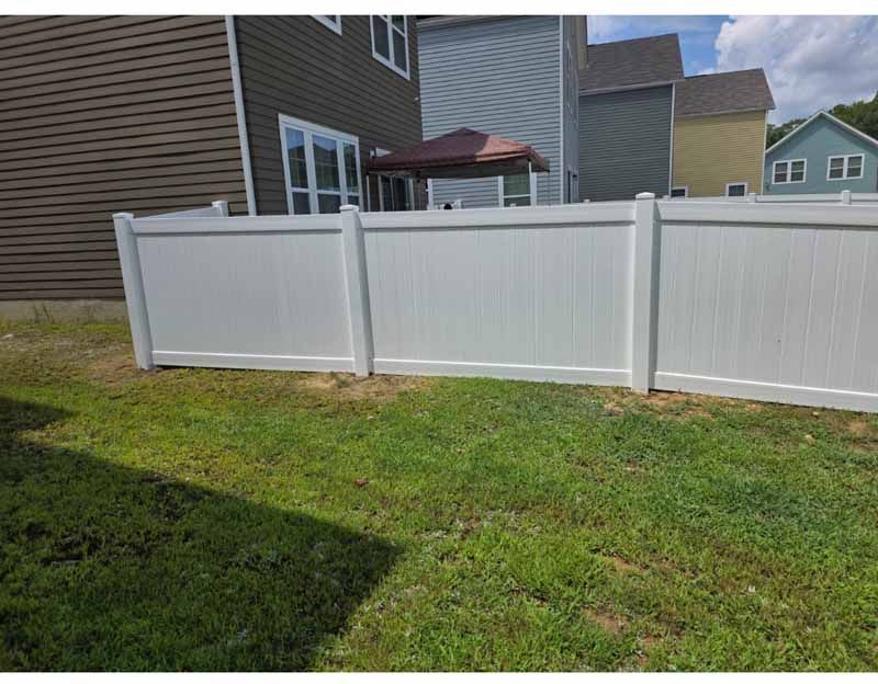 White vinyl privacy fence along a grassy backyard beside a house and patio umbrella
