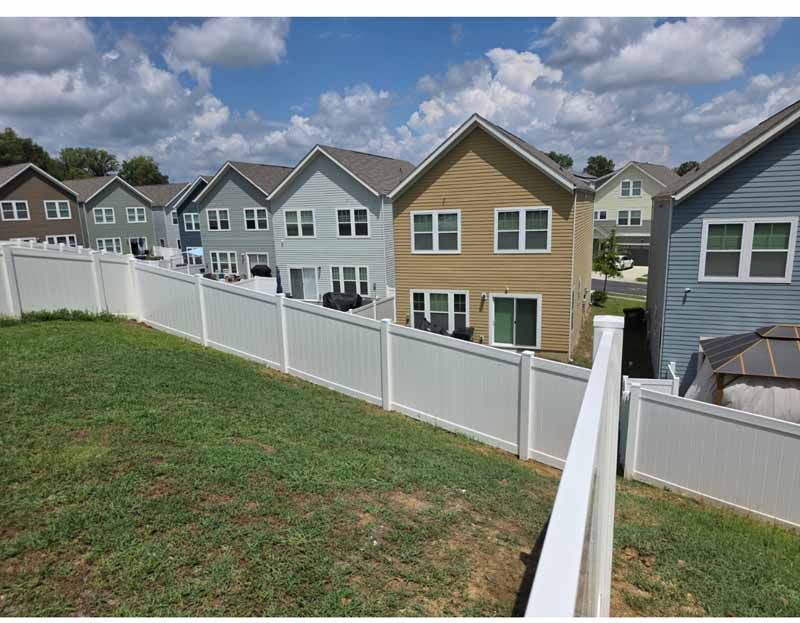 Backyard view of row houses behind a white fence under a cloudy sky