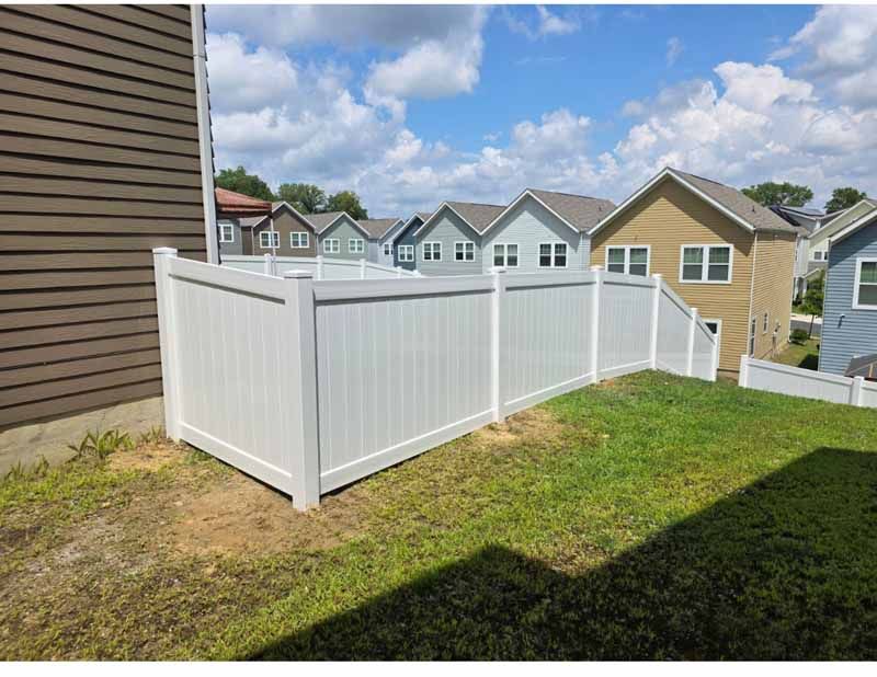 White vinyl fence enclosing a grassy yard beside a brown house, with suburban homes in the background