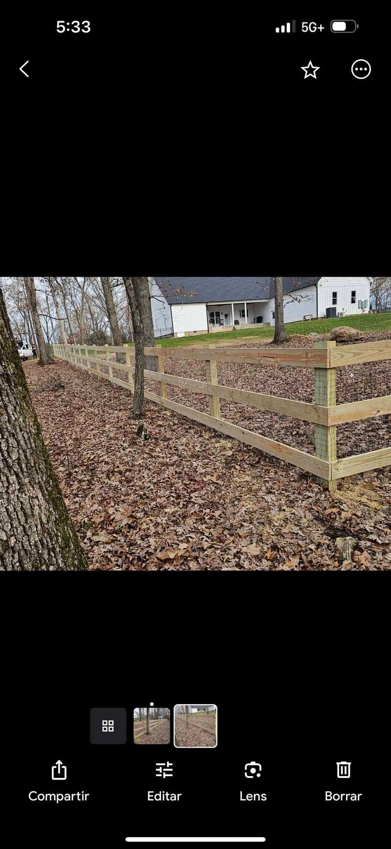 Leaf-covered yard with a weathered wooden fence and bare trees in front of a house.