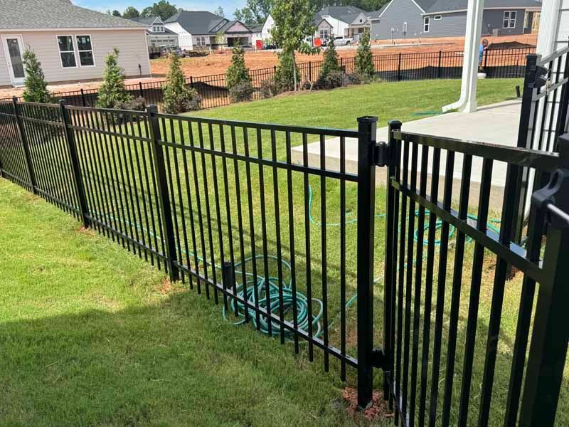 Black metal fence bordering a sloped grassy yard in a suburban neighborhood