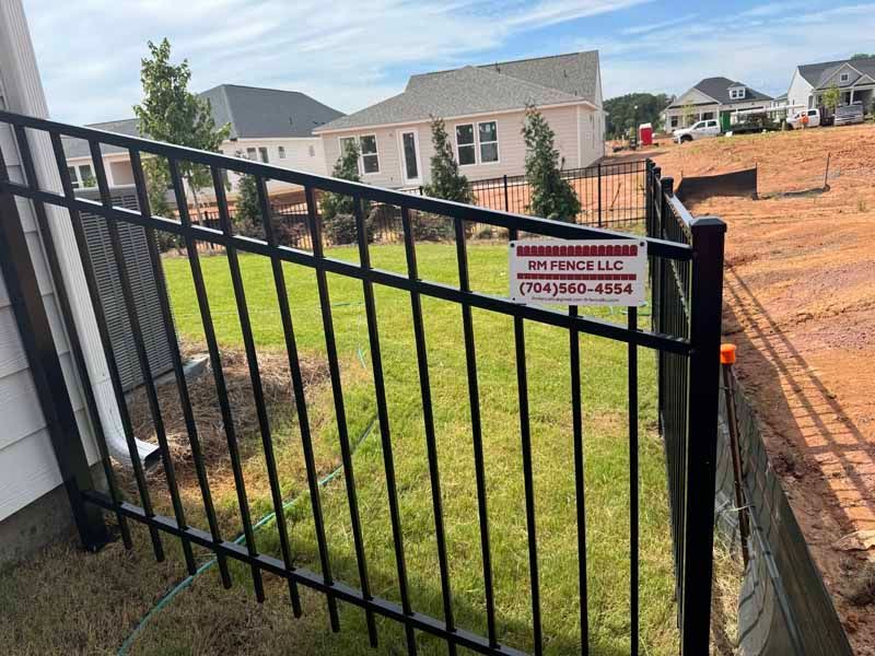 Black metal gate with sign in front of a grassy yard and brick homes under construction