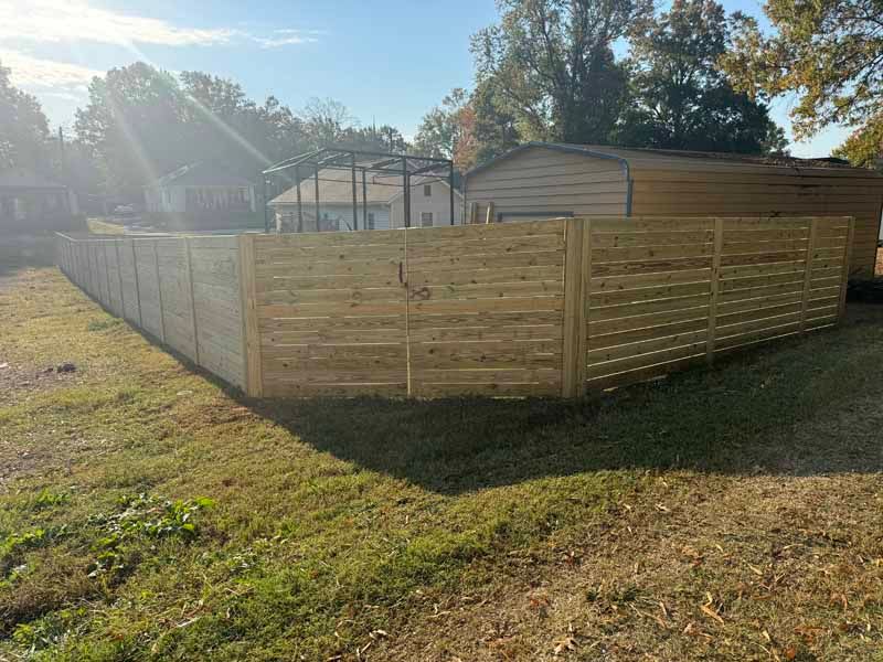 Wooden privacy fence enclosing a yard beside a house, lit by bright afternoon sun.