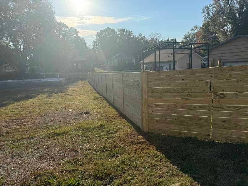 Sunlit backyard with a long wooden privacy fence and grassy yard beside a house