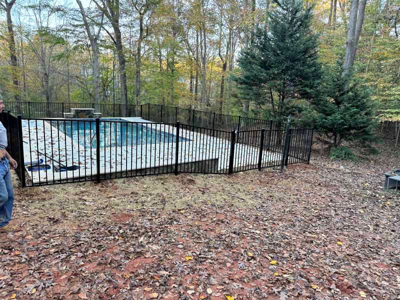 Backyard pool enclosed by black fence, surrounded by autumn trees and fallen leaves