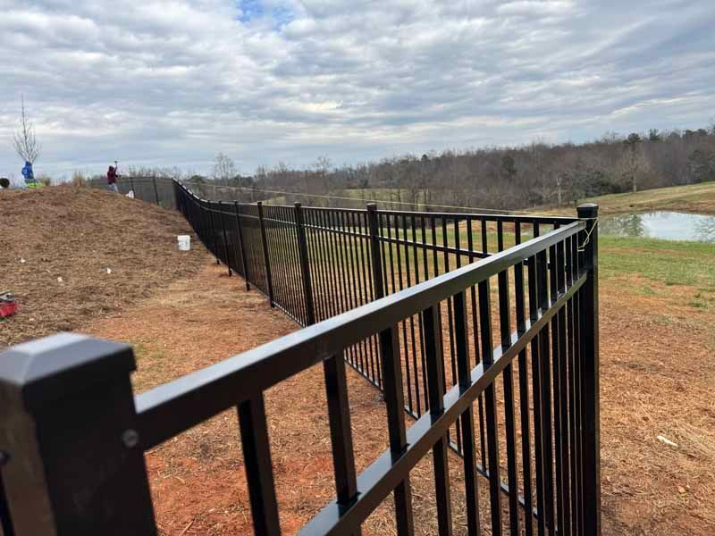 Black metal fence along a dirt path beside a river under a cloudy sky