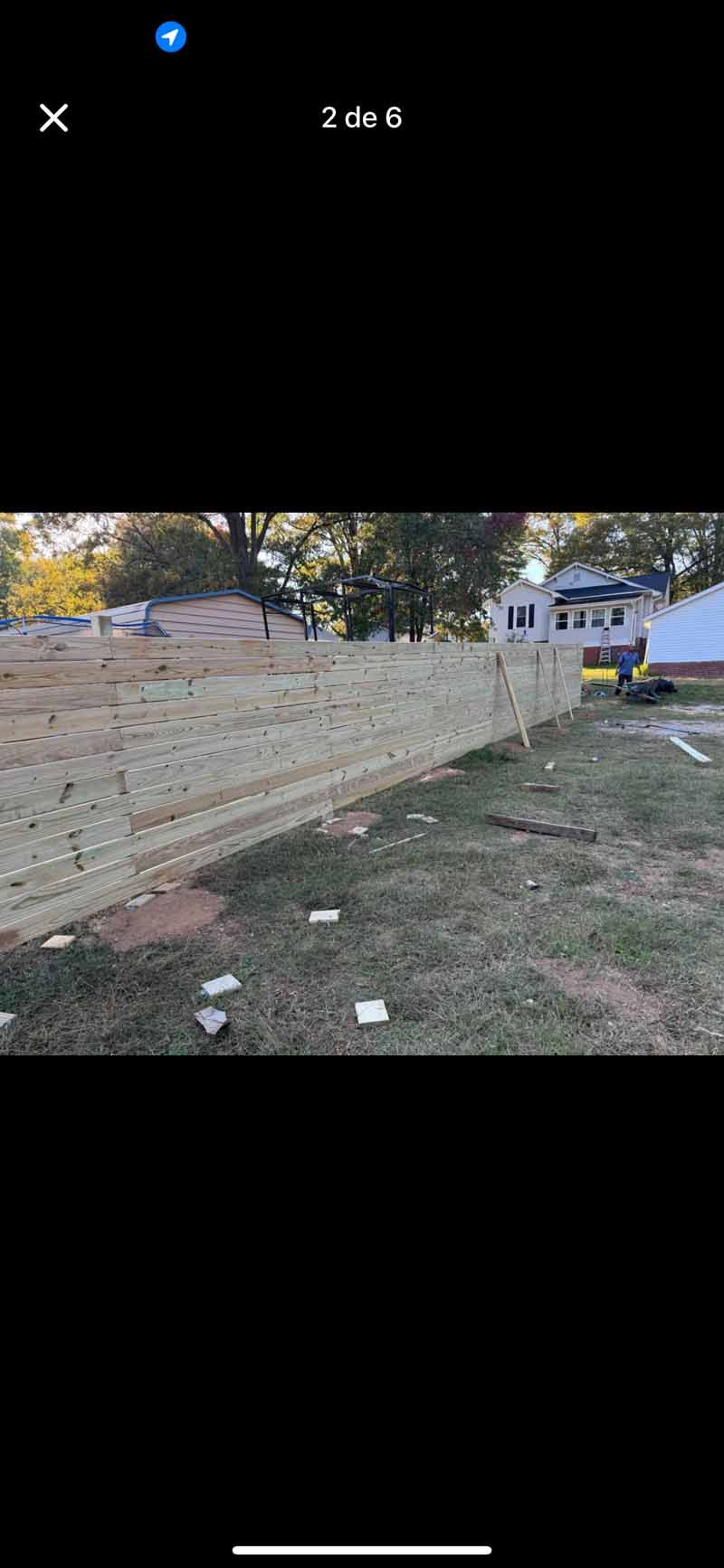 Brick wall beside grassy yard with trees and a white building in the background