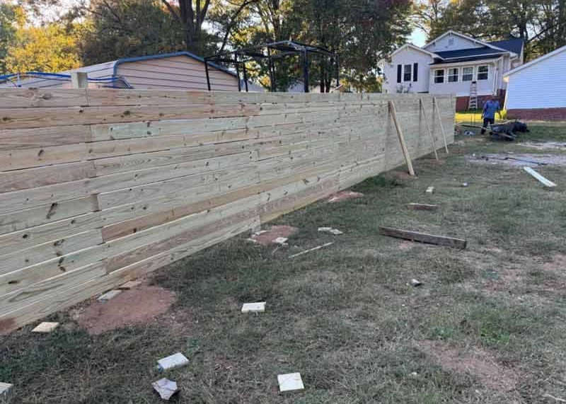 Long wooden privacy fence under construction in a grassy yard with houses in the background