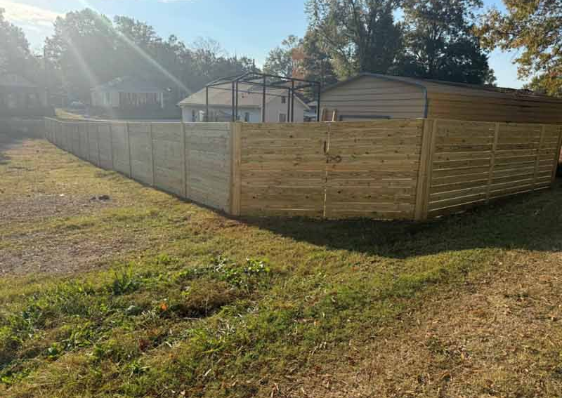Wooden privacy fence around a yard beside a house in a sunny grassy area