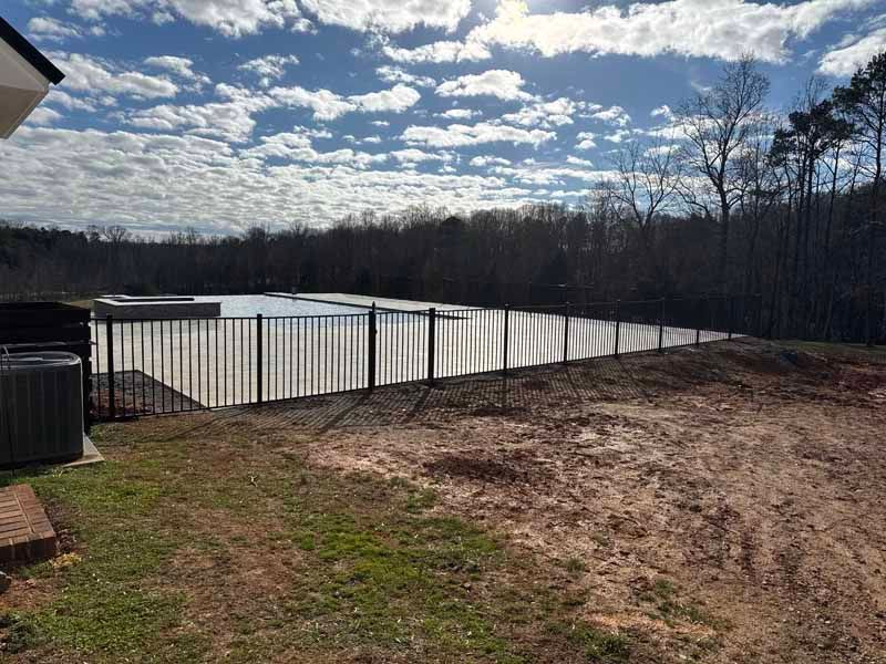 Rural backyard with a covered swimming pool, dirt ground, and cloudy sky over trees
