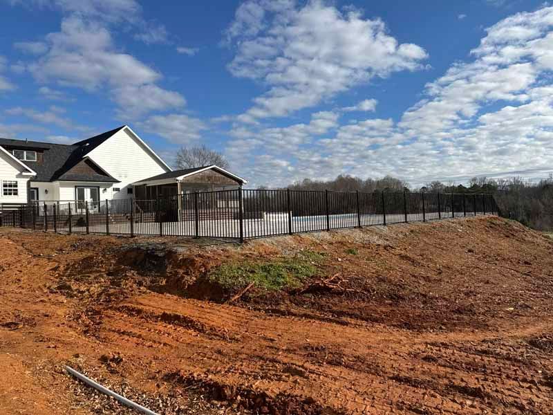 New house under construction beside a fenced dirt lot under a partly cloudy blue sky