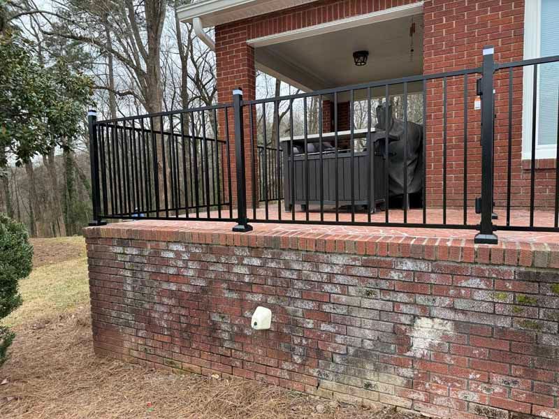 Brick porch with black metal railing and covered patio outside a brick house.