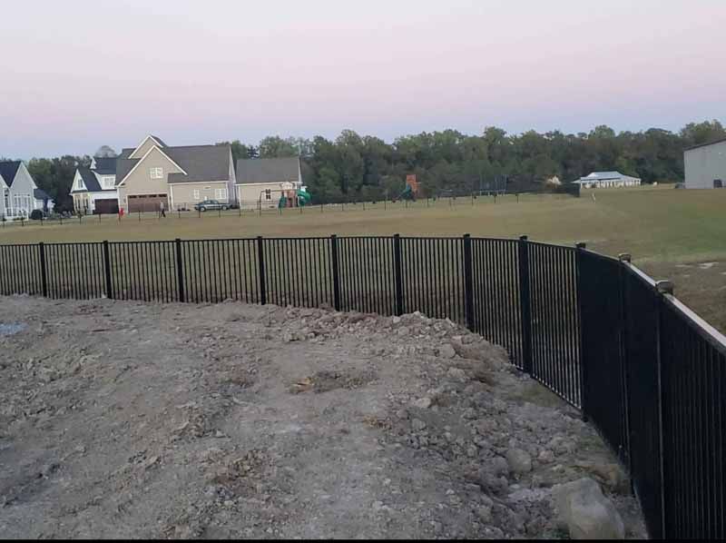 Construction site with silt fence around a dirt excavation near houses and a grassy field