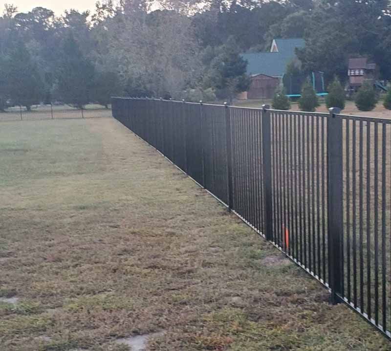 Black metal fence along a grassy field beside a suburban home at dusk