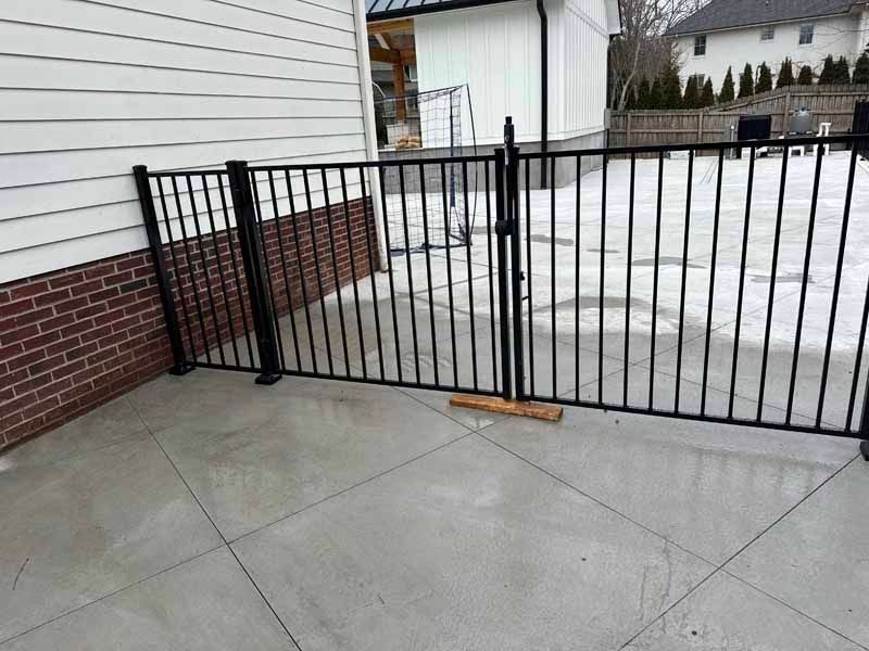 Black metal gate blocking a concrete driveway beside a brick-and-white house in winter