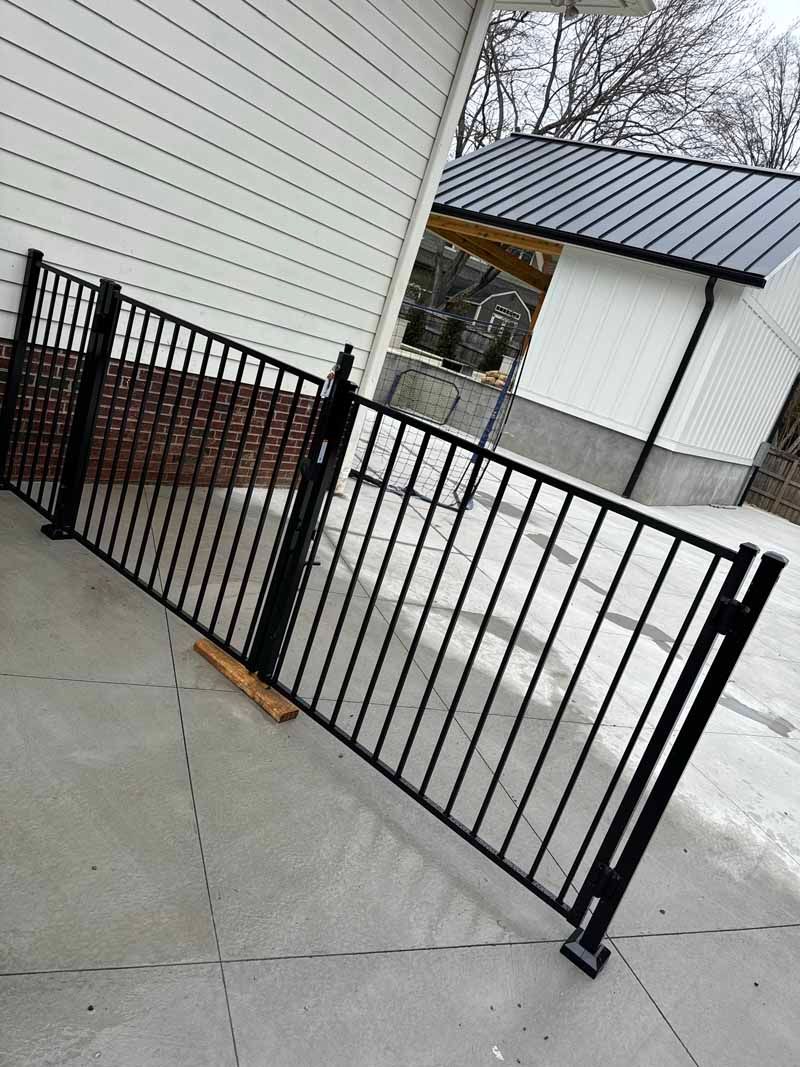 Black metal gate blocking a concrete walkway beside a white building and snowy ground