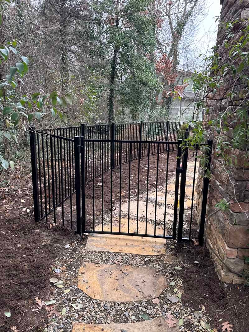 Black metal gate blocking a narrow stone path in a wooded yard