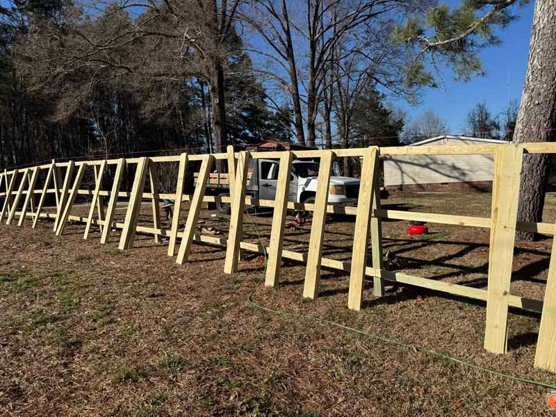 Row of wooden A-frame supports along a dirt path beside trees under a blue sky