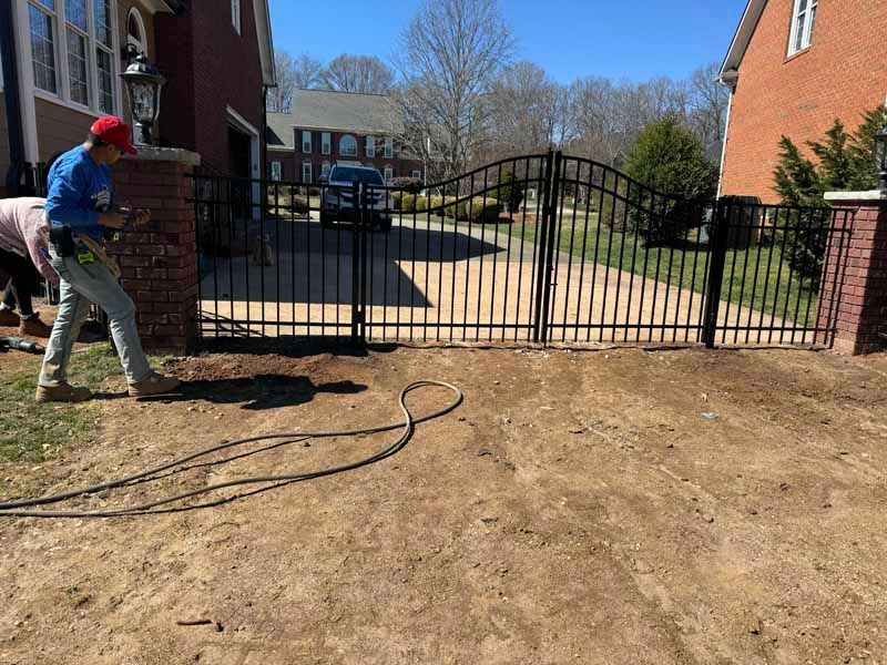 Worker using a pressure washer near a gated apartment courtyard on a sunny day
