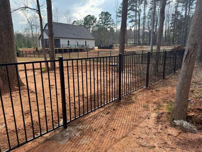 Black metal fence along a wooded yard with a house in the background
