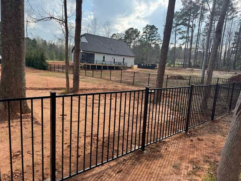Black metal fence in a wooded yard with a white house in the background