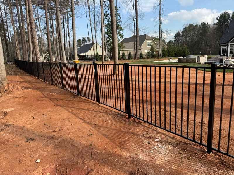 Black metal fence along a red dirt roadside beside a suburban construction area