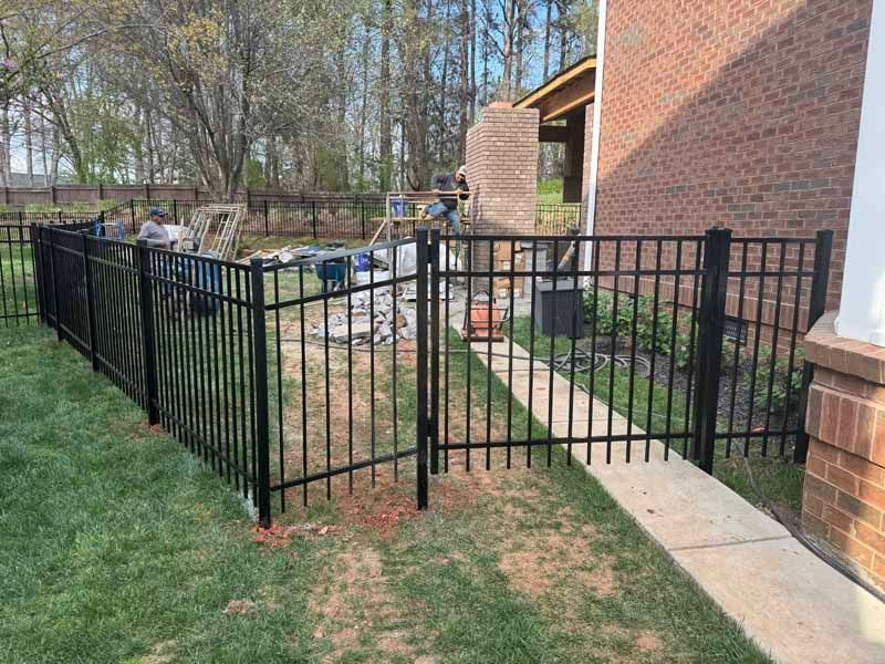 Black metal fence enclosing a walkway beside a brick building and grassy yard.